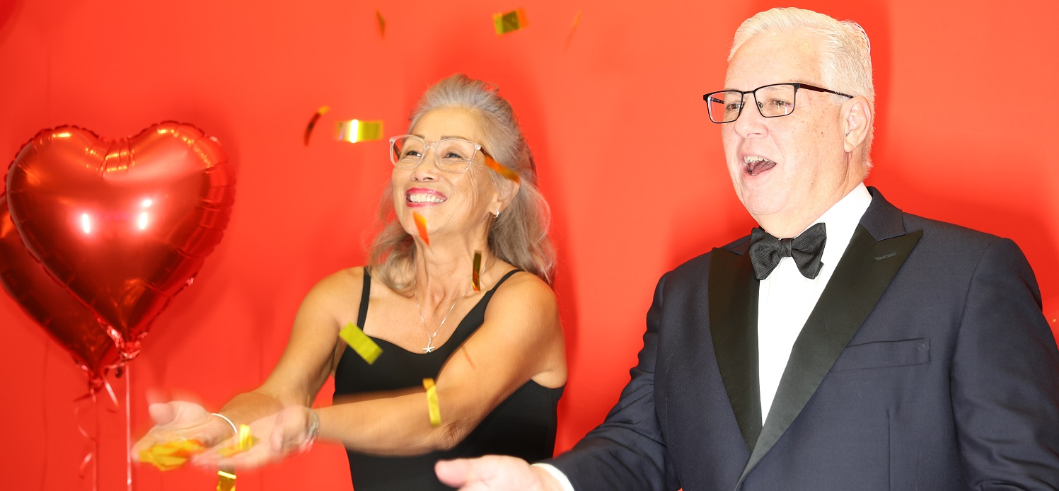 Couple with red heart balloon trying to catch gold confetti